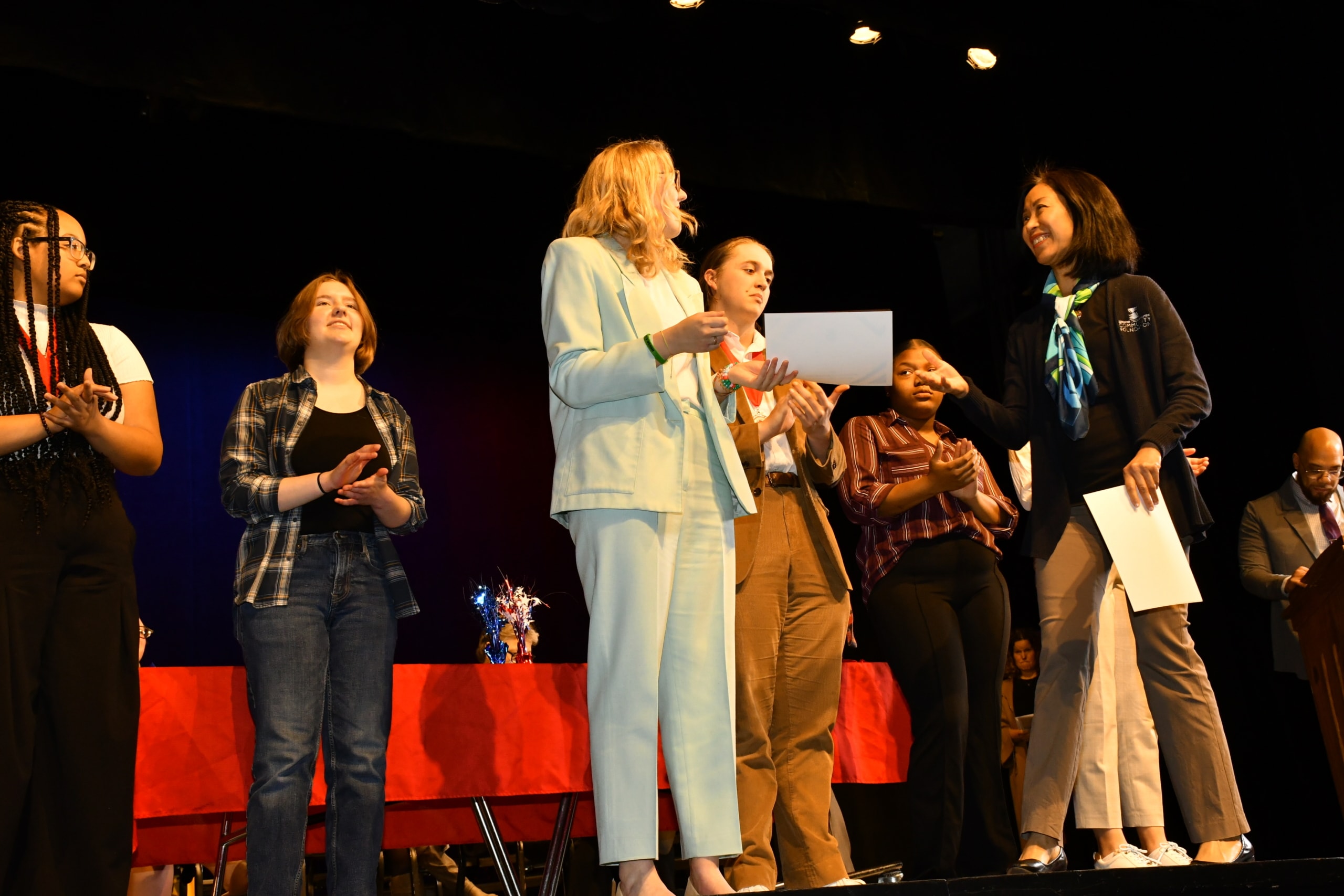 A photo of students on stage while one of them receives a scholarship.