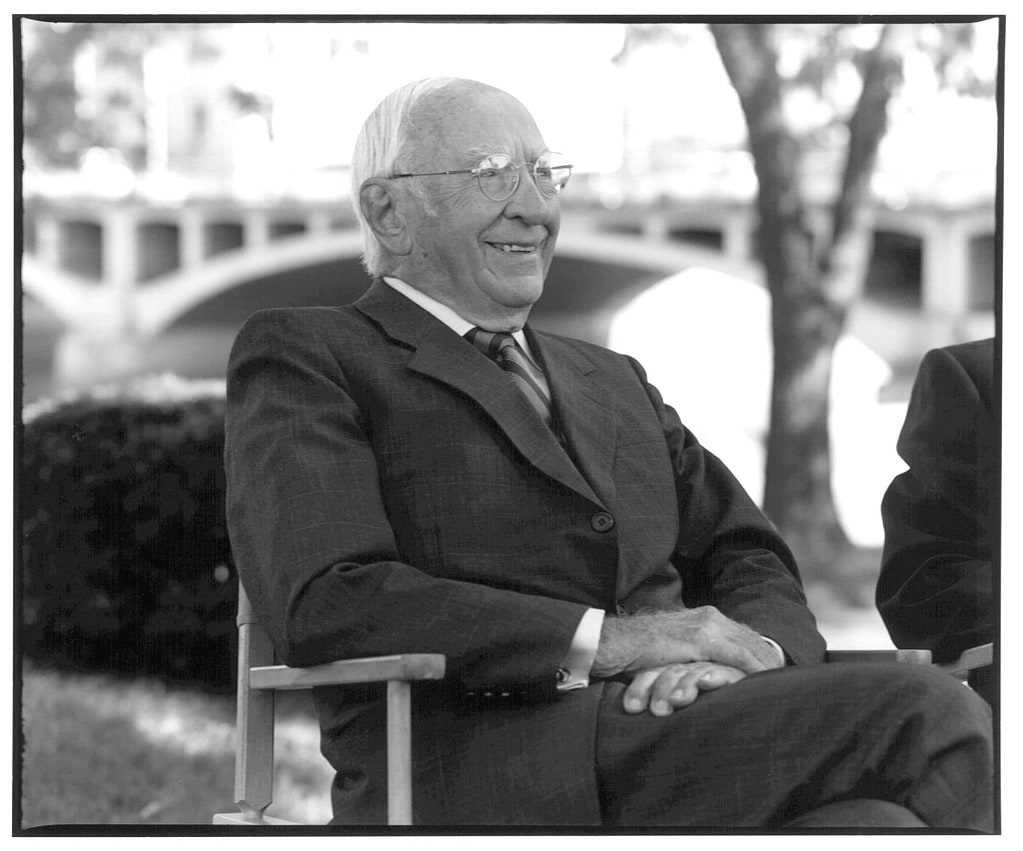 A black and white photo of William Quarton smiling and sitting in a chair outside.