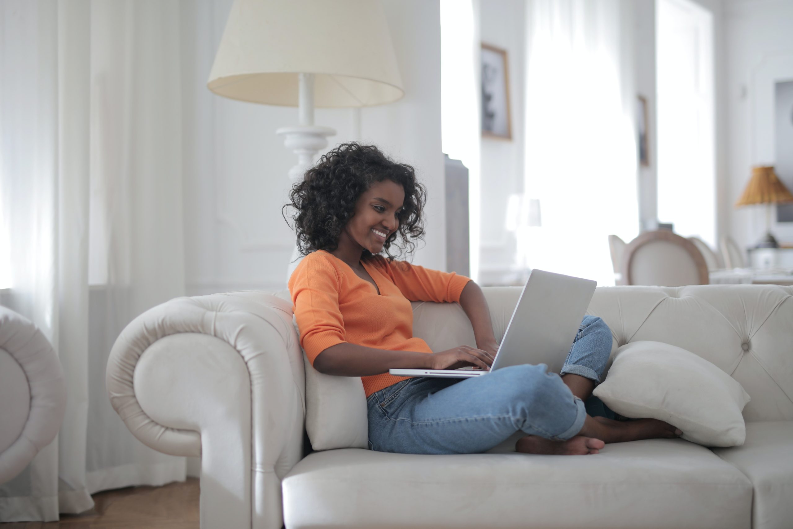 Photo of smiling woman sitting on a couch with a laptop.