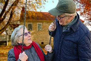 Photo of woman in swing smiling at a man standing next to her.