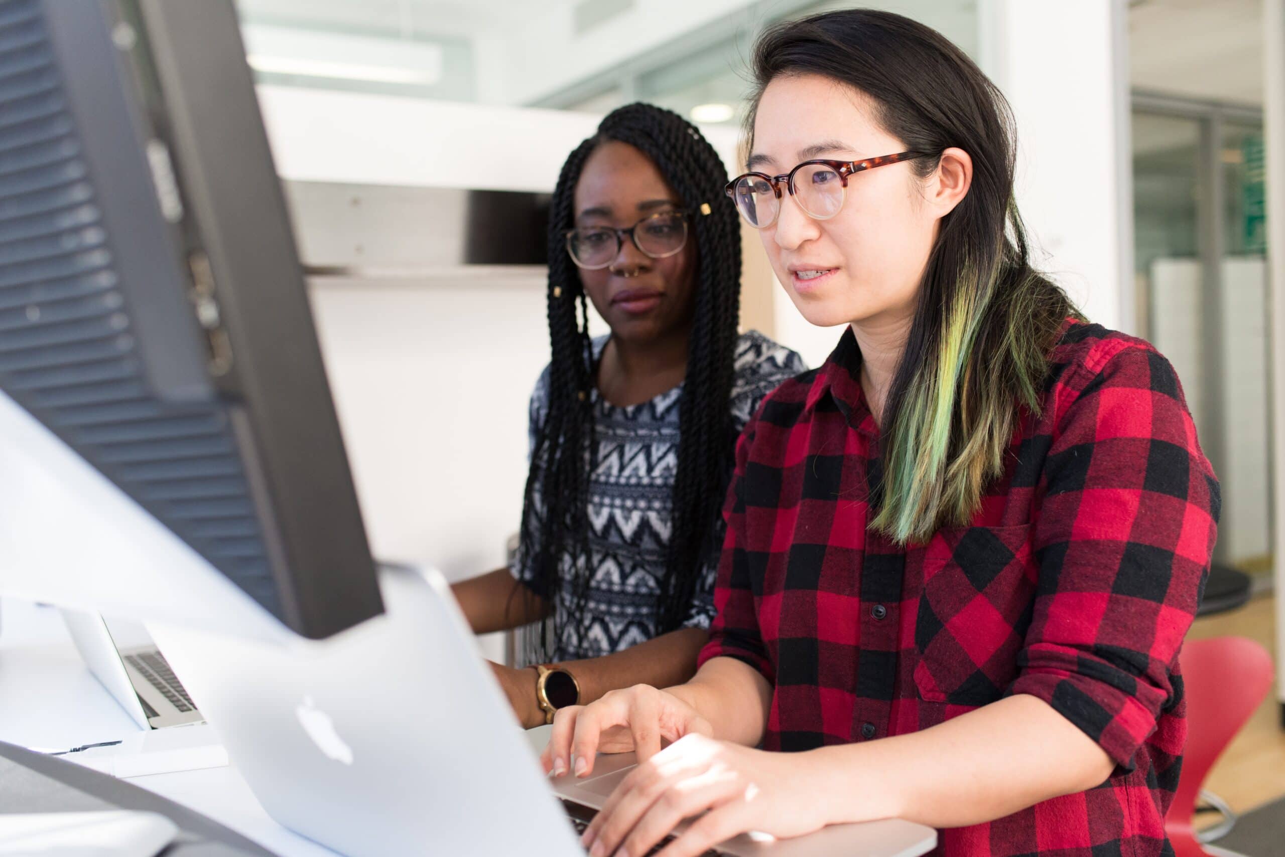 Photo of two women working collaborating on a computer.