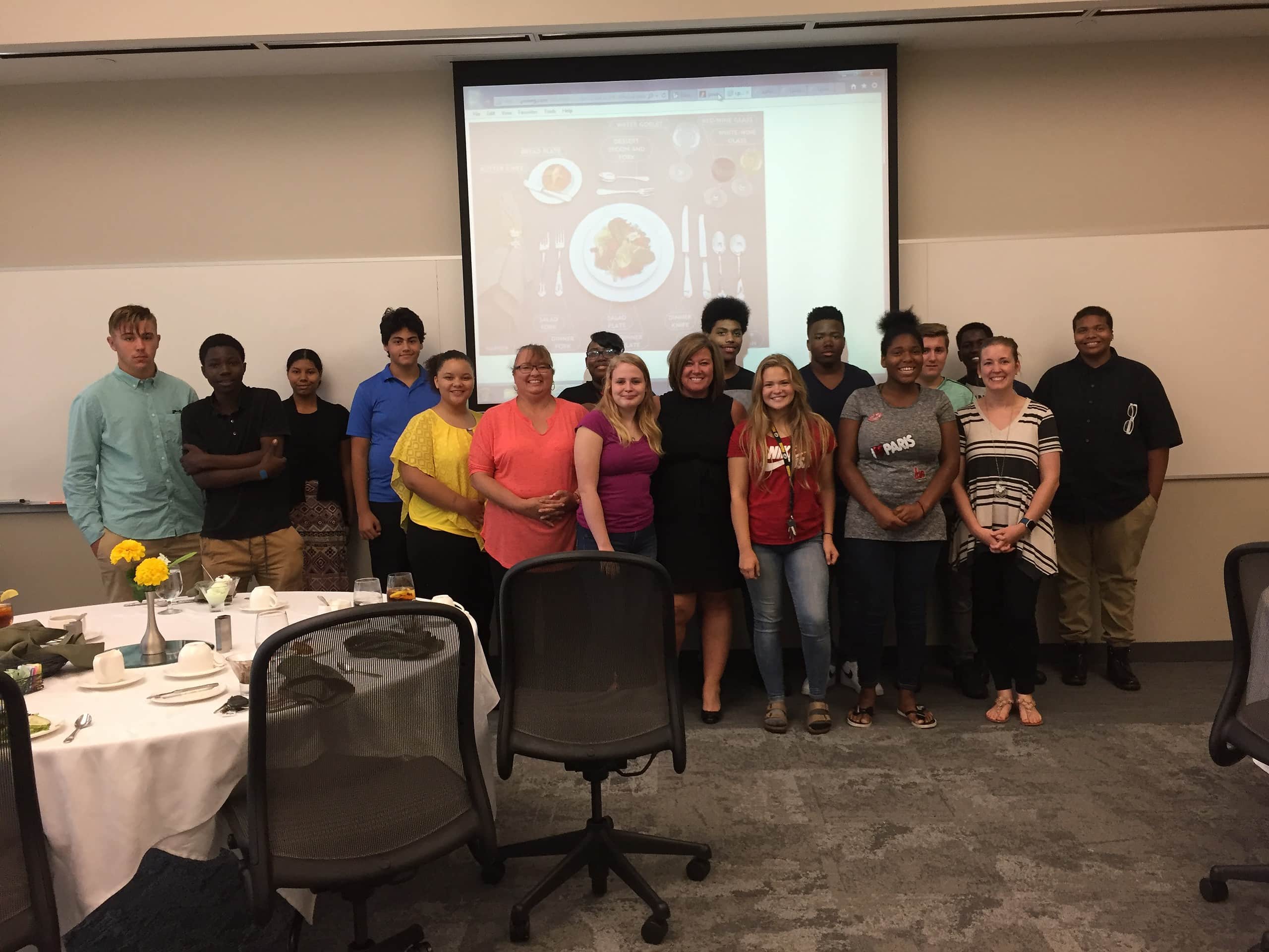 Group of teenagers and middle aged adults posing in front of a projector screen.